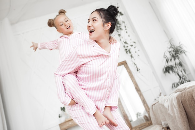 Jonge actieve moeder en haar dochtertje plezier samen thuis in de slaapkamer met pyjama