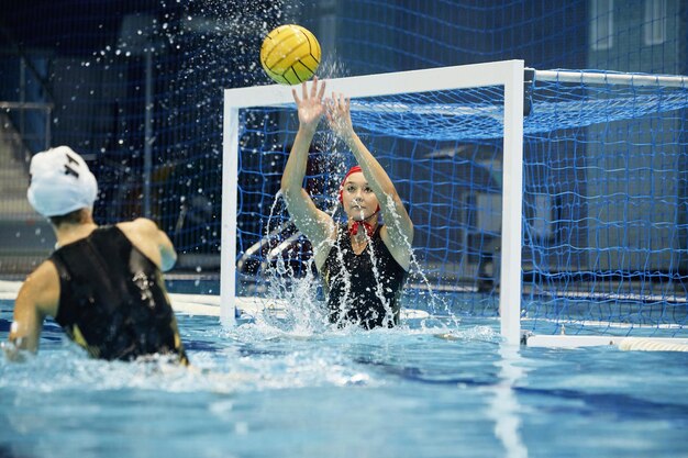 Jonge actieve vrouw in zwembroek spat water en vangt de bal