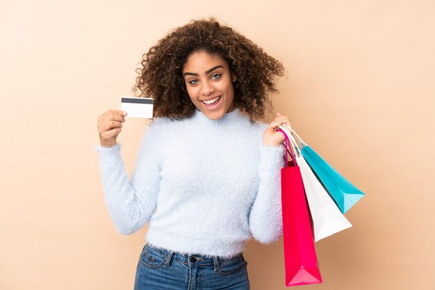 Jonge african american vrouw geïsoleerd op beige boodschappentassen houden en een creditcard