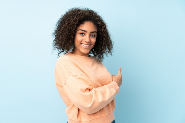 Jonge African American vrouw geïsoleerd op blauw terug te wijzen