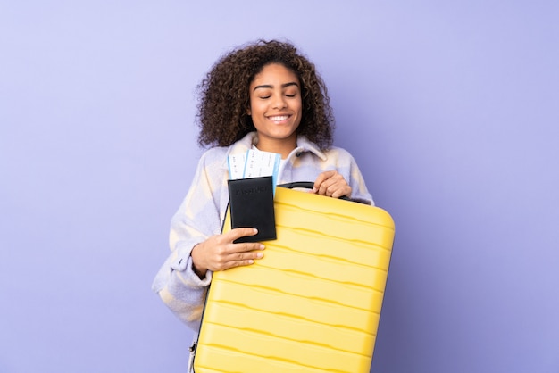 Jonge African American vrouw geïsoleerd op paars in vakantie met koffer en paspoort