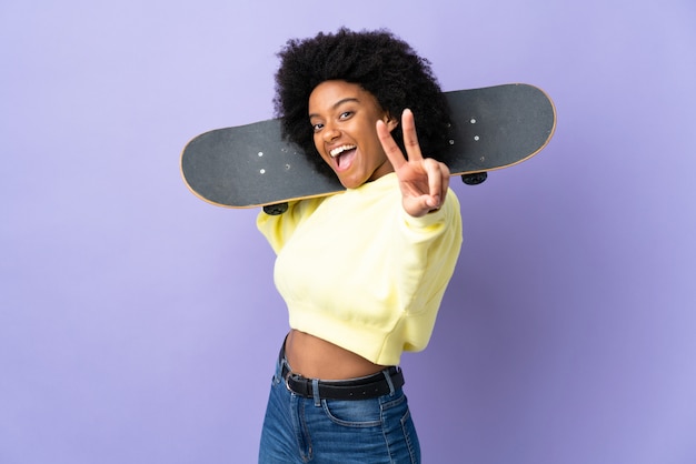 Jonge African American vrouw geïsoleerd op paars met een skate overwinning gebaar doen