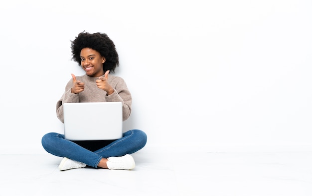 Jonge African American vrouw met een laptop zittend op de vloer geïsoleerd