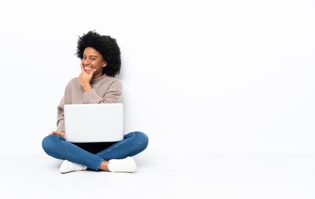 Jonge African American vrouw met een laptop zittend op de vloer lachend