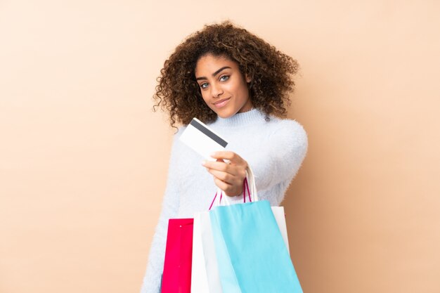 Jonge African American vrouw op beige muur boodschappentassen houden en een creditcard