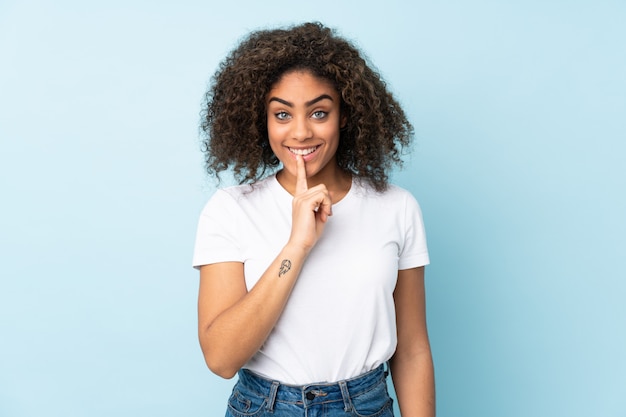 Jonge African American vrouw op blauwe muur met een teken van stilte gebaar vinger in mond zetten