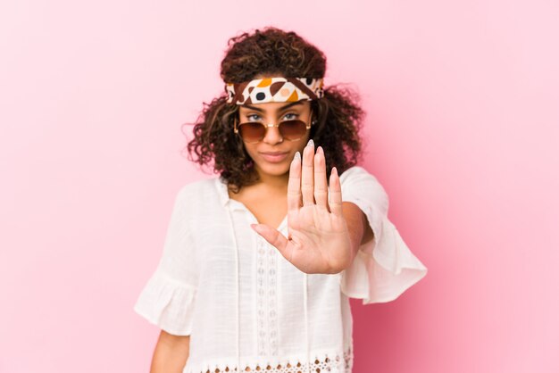 Jonge Afrikaanse Amerikaanse hipstervrouw die op roze muur wordt geïsoleerd die zich met uitgestrekte hand bevinden die eindeteken tonen, die u verhinderen.
