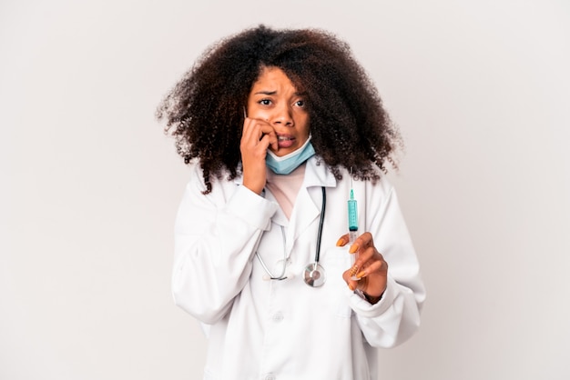 Jonge afrikaanse amerikaanse krullende artsenvrouw die een spuit houdt die vingernagels bijt, zenuwachtig en zeer angstig.