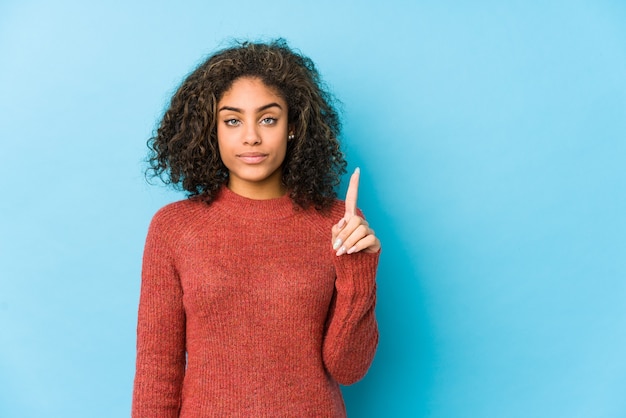 Jonge Afrikaanse Amerikaanse krullende haarvrouw die nummer één met vinger toont.