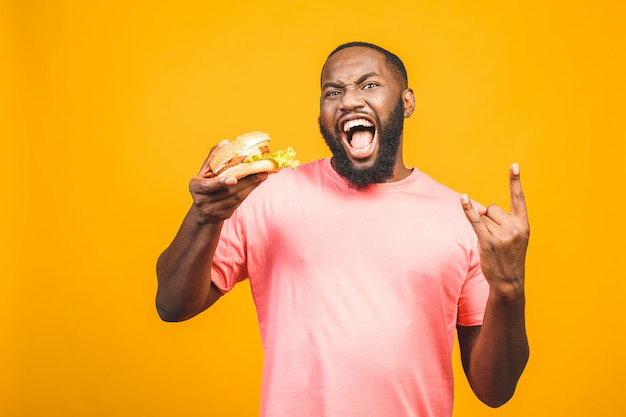 Jonge Afrikaanse Amerikaanse mens die hamburger eet die over gele muur wordt geïsoleerd.