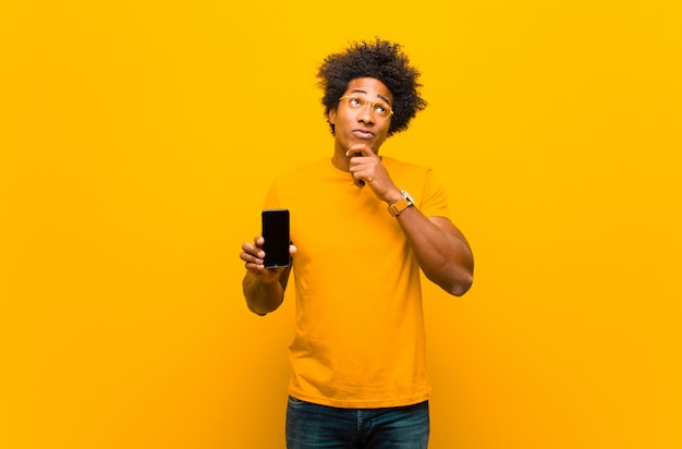 Jonge Afrikaanse Amerikaanse mens met een slimme telefoon tegen sinaasappel