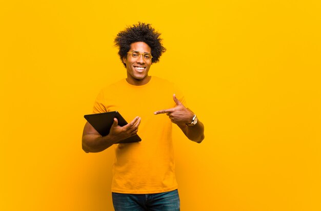 Jonge Afrikaanse Amerikaanse mens met een tablet tegen oranje backgrou