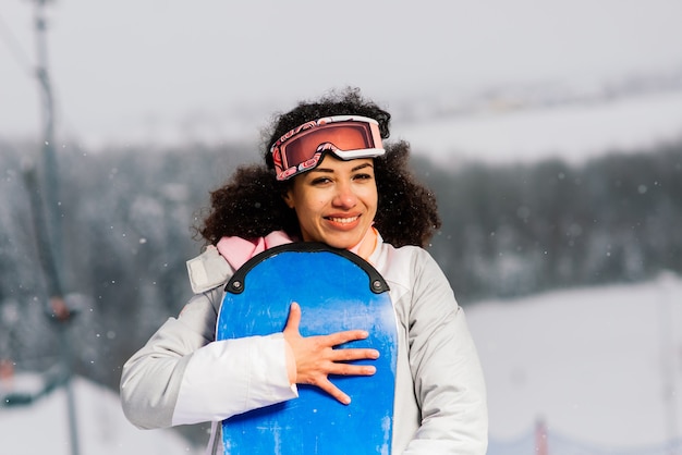 Jonge afrikaanse amerikaanse skiërvrouw die met snowboard en duim glimlachen opheffen