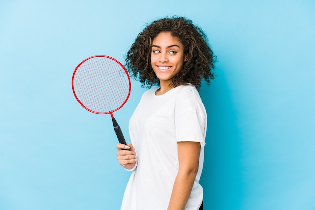Jonge afrikaanse amerikaanse vrouw die badminton speelt kijkt opzij glimlachend, vrolijk en aangenaam.