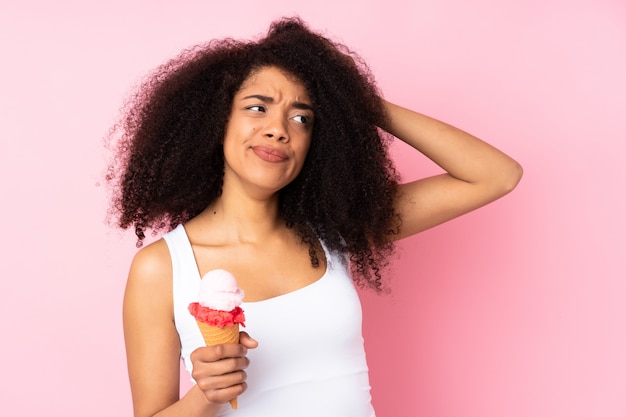 Jonge Afrikaanse Amerikaanse vrouw die een kornetijs houdt dat op roze wordt geïsoleerd dat twijfels heeft en met gezichtsuitdrukking verwart