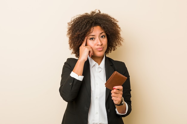 Jonge Afrikaanse Amerikaanse vrouw die een portefeuille houdt die zijn tempel met vinger richt, het denken, concentreerde zich op een taak.