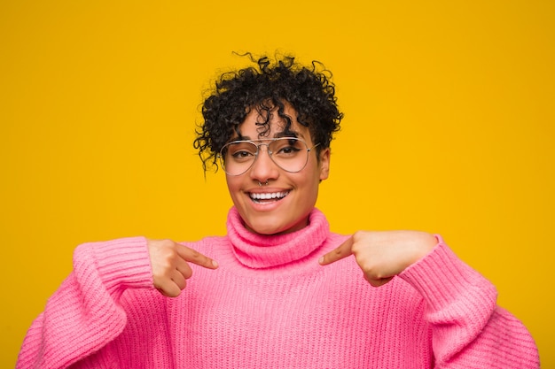 Jonge afrikaanse amerikaanse vrouw die een roze sweater draagt verrast het richten met vinger, breed glimlachend.