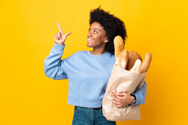 Jonge Afrikaanse Amerikaanse vrouw die iets brood koopt dat op gele achtergrond wordt geïsoleerd die met de wijsvinger een groot idee richt