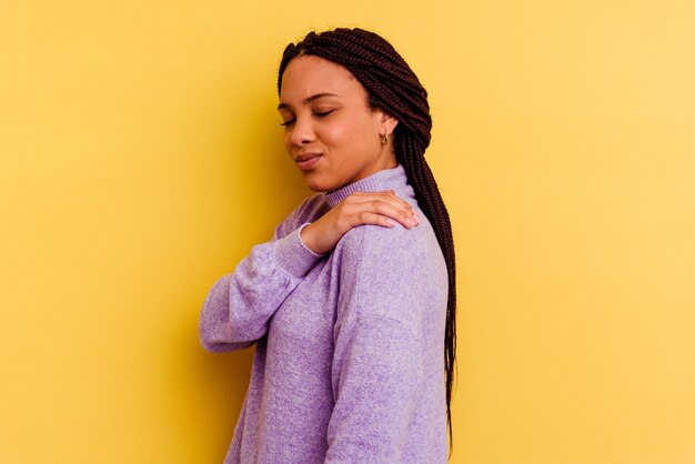 Foto jonge afrikaanse amerikaanse vrouw die op gele muur wordt geïsoleerd die een schouderpijn heeft.