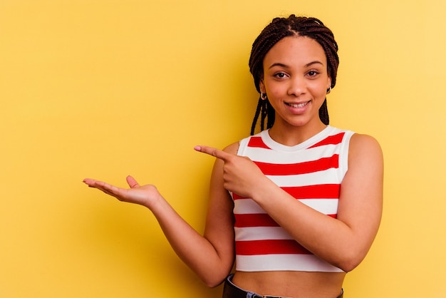 Jonge afrikaanse amerikaanse vrouw die op gele muur wordt geïsoleerd die opgewonden houdt een exemplaarruimte op palm.