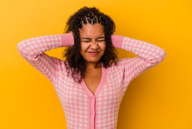 Jonge afrikaanse amerikaanse vrouw die op gele muur wordt geïsoleerd die oren behandelt met handen die niet te hard geluid proberen te horen.