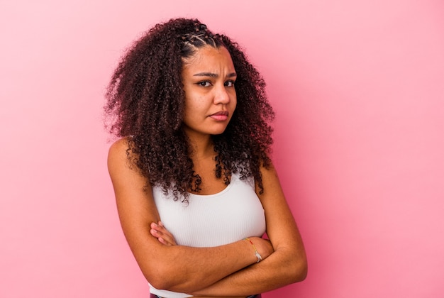 Jonge afrikaanse amerikaanse vrouw die op roze muur wordt geïsoleerd die ongelukkig kijkt met sarcastische uitdrukking.