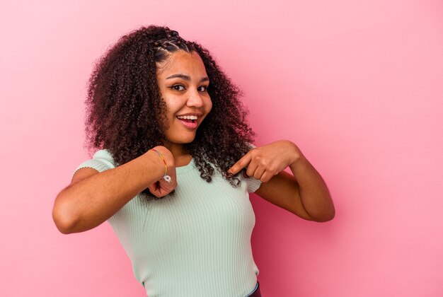 Jonge afrikaanse amerikaanse vrouw die op roze muur wordt geïsoleerd verrast wijzend met vinger, breed glimlachend