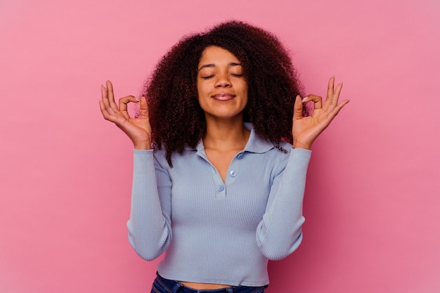 Jonge afrikaanse amerikaanse vrouw die op roze wordt geïsoleerd ontspant na een zware werkdag, zij voert yoga uit.