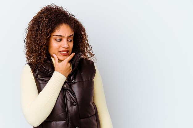 Jonge afrikaanse amerikaanse vrouw die op witte muur wordt geïsoleerd die achterkant van het hoofd raakt, denkt en een keus maakt.