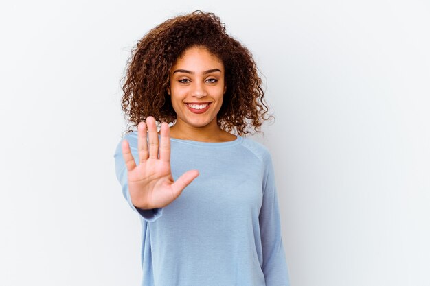 Jonge afrikaanse amerikaanse vrouw die op witte muur wordt geïsoleerd die vrolijk glimlachen toont nummer vijf met vingers.