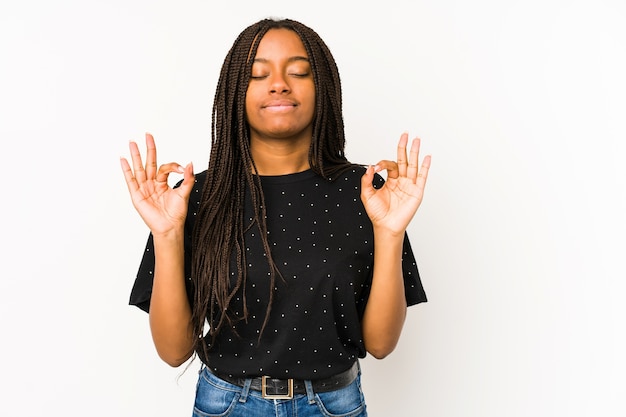 Jonge afrikaanse amerikaanse vrouw die op witte muur wordt geïsoleerd ontspant na een zware werkdag, zij voert yoga uit.