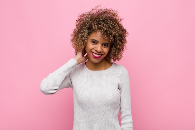 Jonge Afrikaanse Amerikaanse vrouw die vrolijk en vol vertrouwen met een toevallige, gelukkige, vriendelijke glimlach tegen roze muur lacht
