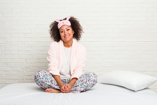 Jonge Afrikaanse Amerikaanse vrouw in het bed dat gelukkig, vrolijk en vrolijk pijama draagt.