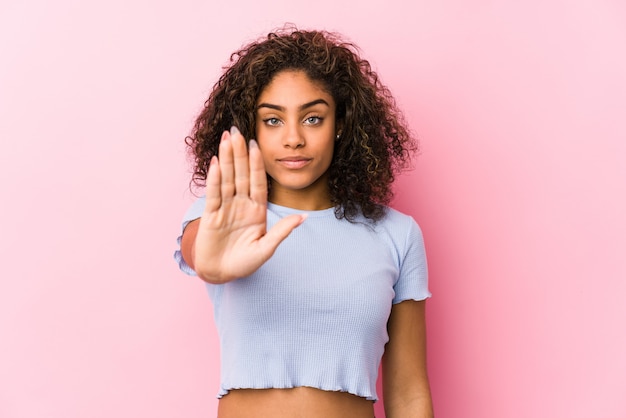 Jonge Afrikaanse Amerikaanse vrouw tegen een roze muur die zich met uitgestrekte hand bevindt die eindeteken toont, dat u verhindert.