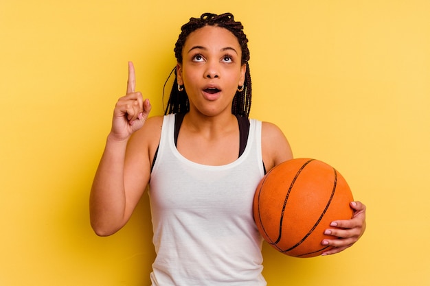 Jonge afrikaanse amerikaanse vrouwen speelbasketbal die op gele muur wordt geïsoleerd die ondersteboven met geopende mond richt.