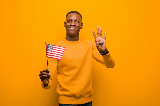 Jonge Afrikaanse Amerikaanse zwarte mens die tegen oranje muur een vlag van de VS houdt