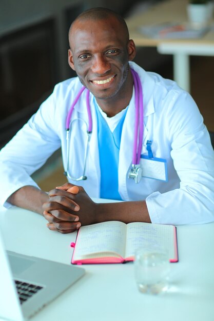 Jonge Afrikaanse arts die aan laptop bij bureau werkt