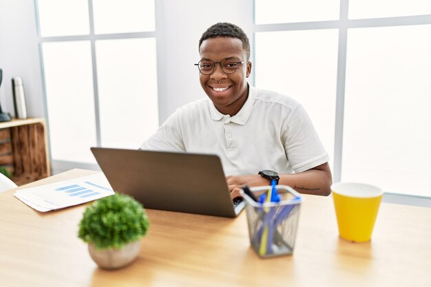 Jonge afrikaanse man aan het werk op kantoor met behulp van een computerlaptop met een vrolijke en coole glimlach op het gezicht. mens met veel geluk.