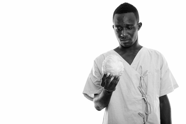 jonge Afrikaanse man als ziekenhuispatiënt geïsoleerd tegen witte muur in zwart en wit