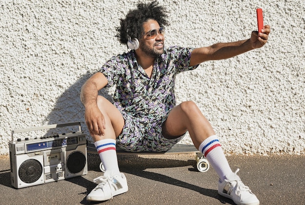 Foto jonge afrikaanse man die een selfie maakt terwijl hij op een skateboard zit en muziek luistert van vintage boombox