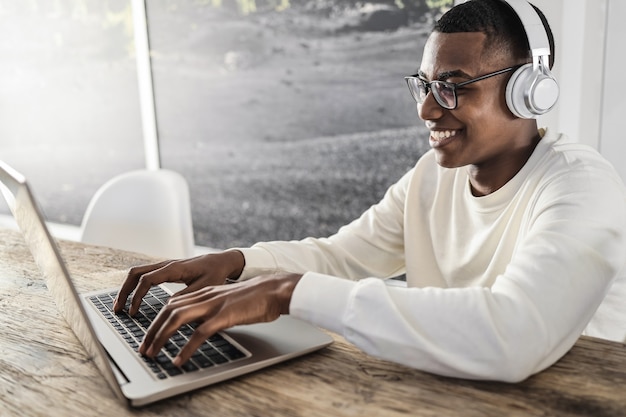 Jonge afrikaanse man die laptopcomputer gebruikt terwijl hij thuis een koptelefoon draagt - focus op gezicht