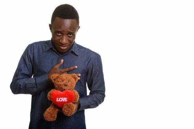 Jonge Afrikaanse man kijkt verdrietig terwijl hij teddybeer vasthoudt