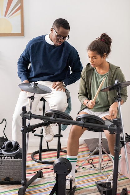 Foto jonge afrikaanse man legt biraciaal schoolmeisje uit hoe ze drumstel moet spelen