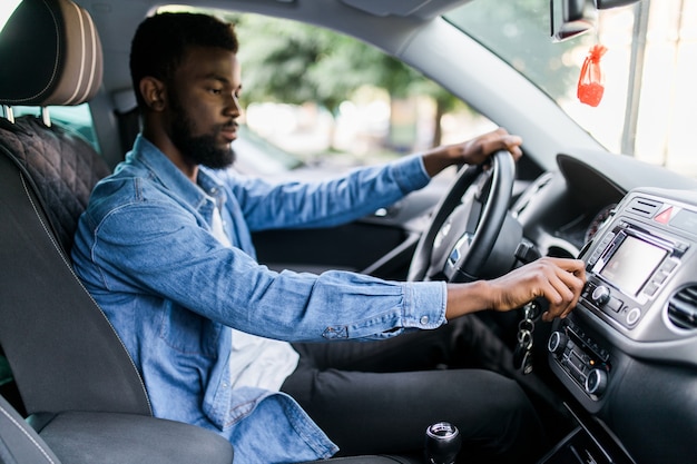 Foto jonge afrikaanse man verandert muziek in de auto tijdens het rijden op de weg