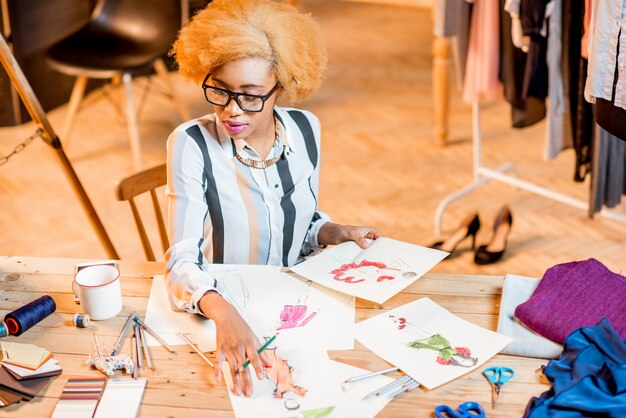 Jonge afrikaanse modeontwerper die werkt met kledingtekeningen die in het kantoorinterieur zitten met verschillende kleermakers