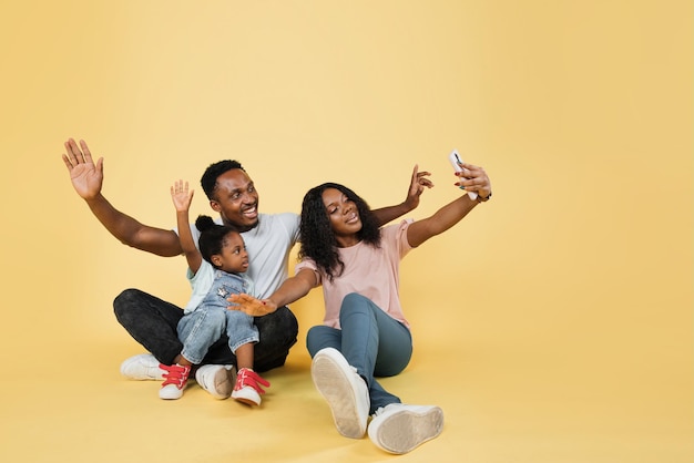 Jonge afrikaanse ouders brengen tijd door met hun dochtertje met open armen en gebruiken de telefoon voor selfie