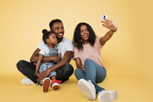 Jonge Afrikaanse ouders zitten op de vloer met hun dochter en omarmen het gebruik van smartphone voor selfie