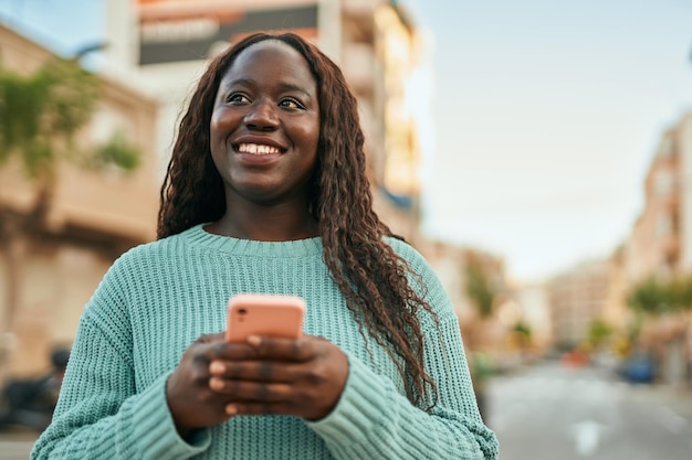 Jonge afrikaanse vrouw die lacht gelukkig met behulp van smartphone in de stad