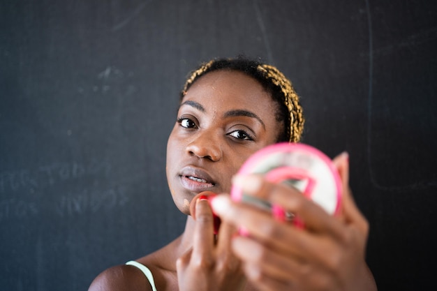 Jonge afrikaanse vrouw die naar de camera kijkt terwijl ze make-up aanbrengt met een spiegel