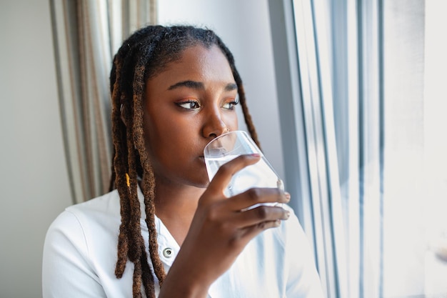 Jonge Afrikaanse vrouw in vrijetijdskleding drinkwater uit glas